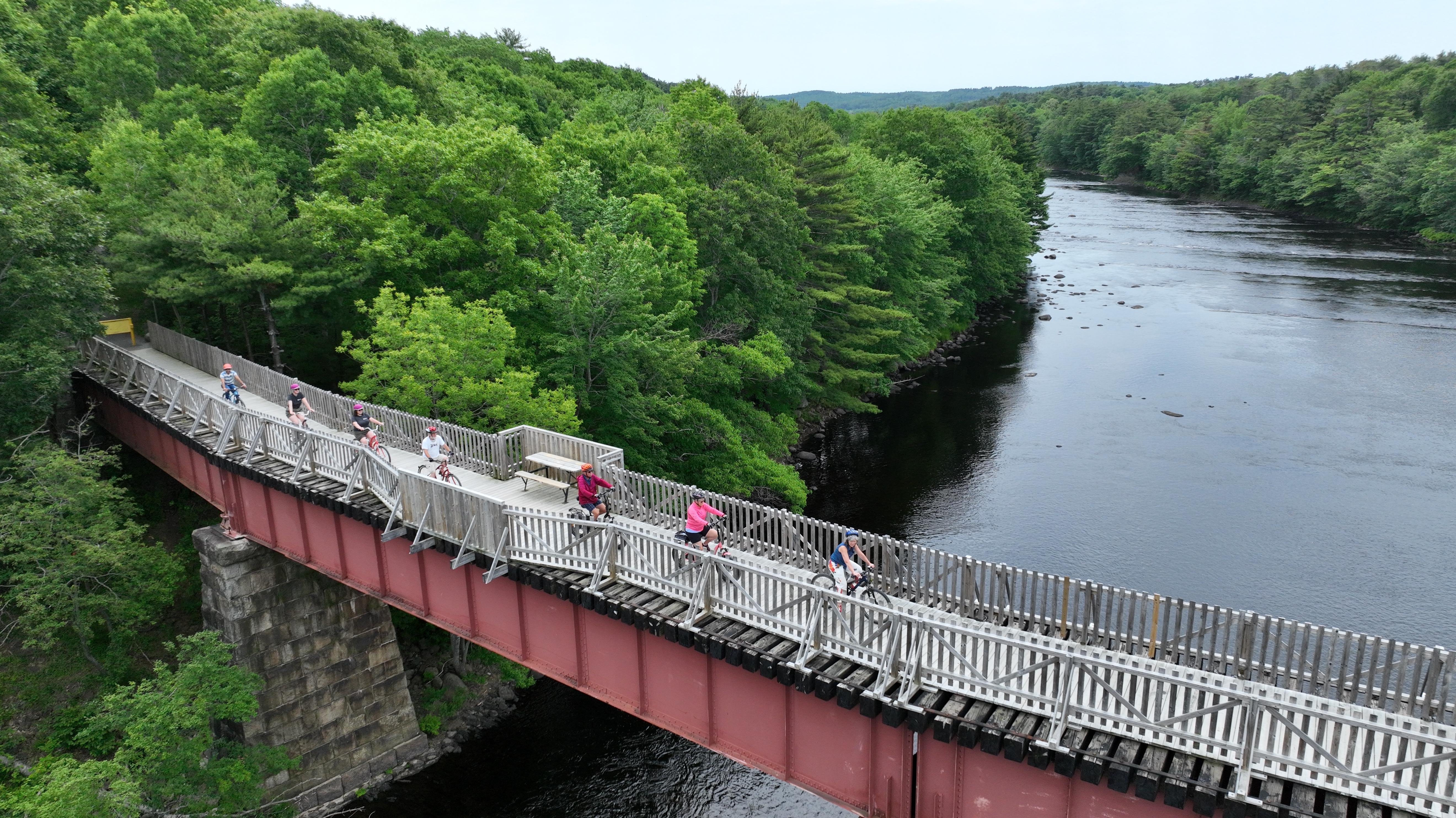 Group riding bikes across the old train bridge on the centennial trail, overlooking the LaHave River in Bridgewater